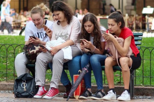 Four girls sitting on a bench and looking at their mobile phones.
