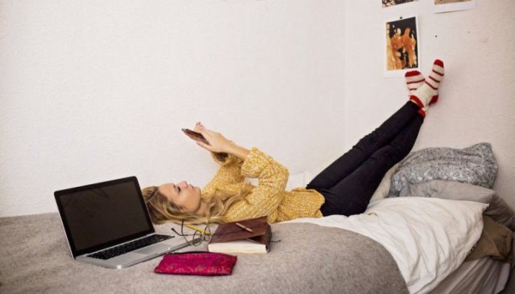 Kvinna som ligger på en säng och kollar sin mobil
