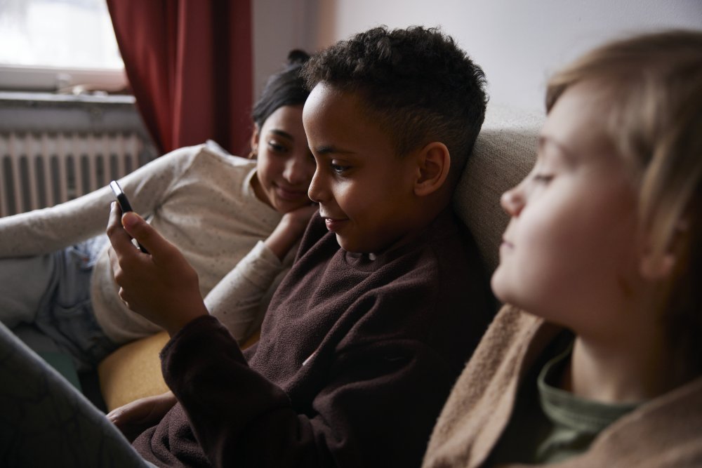 Tre barn som tittar på en smarttelefon i soffan 