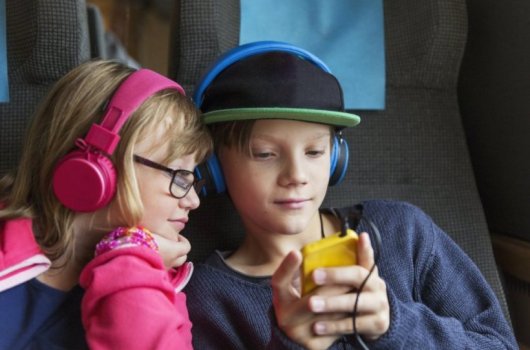 Two kids with headphones watching a cell phone