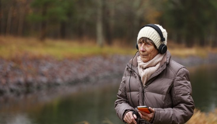 Kvinna i naturen som lyssnar på musik i hörlurar 