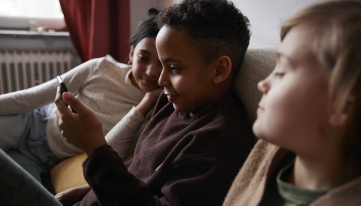 Tre barn som tittar på en smarttelefon i soffan 
