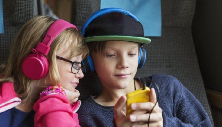 Två barn med hörlurar som tittar på en mobilskärm.